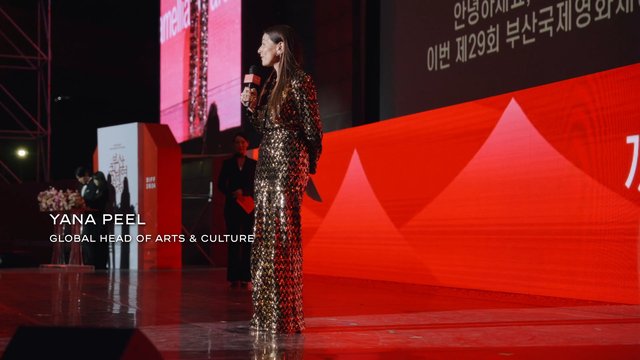 Video Reference: stage, speaker, woman, microphone, event, presentation, red lighting, sequin dress, conference, award ceremony, performance, crowd stage, Korean text, spotlight, formal event