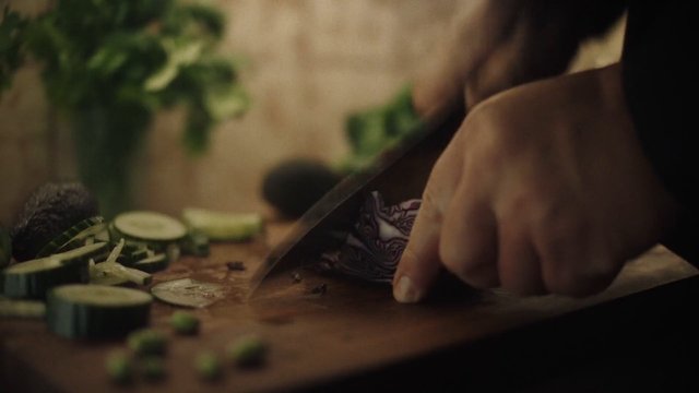 Video Reference: cooking, food prep, vegetables, cucumber, cutting board, knife, hand, kitchen, close-up, slice, fresh produce, meal preparation, home cooking, blurred background