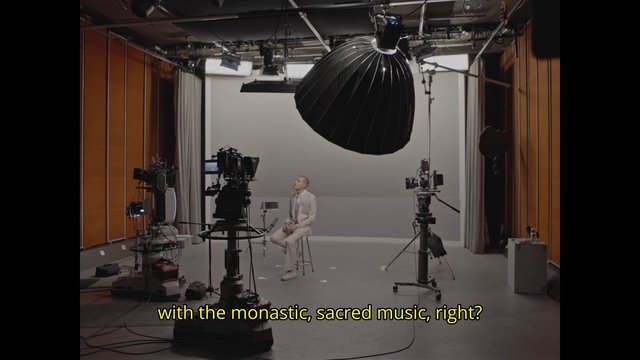 Video Reference: film studio, camera equipment, lighting, interview, seated man, studio set, production gear, green screen, tripod, microphone, subtitles, behind the scenes, broadcast, empty stage, professional video