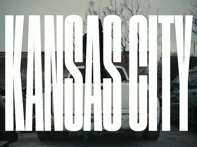 Video Reference: Kansas City, text overlay, pickup truck, parked cars, outdoor, street, urban, vehicle, winter trees, title card, typography, large text