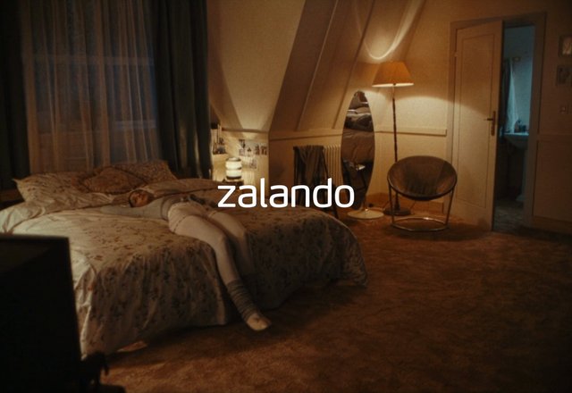Video Reference: bedroom, bed, person lying down, lamp, chair, mirror, doorway, bathroom, curtains, dim lighting, interior, home, nightstand, floor, cozy, residential