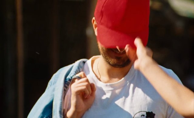 Video Reference: man, red cap, beard, close-up, outdoor, casual clothing, adjusting hat, portrait, shallow depth of field, sunlight