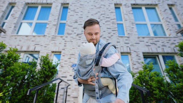 Video Reference: man, baby, infant carrier, outdoors, building, brick wall, windows, parenting, family, steps, urban, daylight, portrait, care, father
