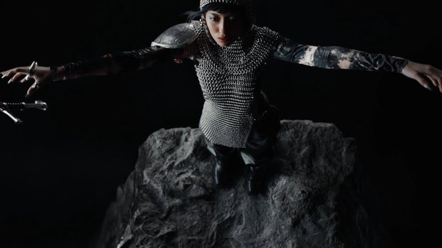 Video Reference: person, fashion, avant-garde, chainmail, dark background, pose, rock, studio lighting, costume, editorial, artistic, dramatic, black, metallic, standing, arms out
