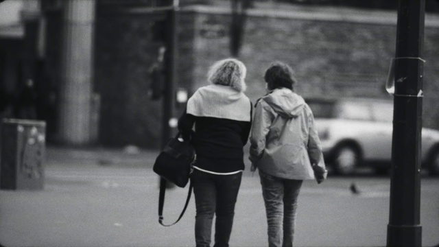 Video Reference: Standing, Black-and-white, Gesture, Street fashion, Grey, Style, Road surface, Luggage and bags, Sidewalk, Monochrome