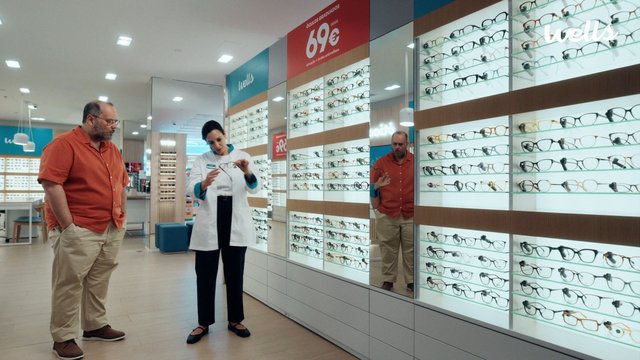 Video Reference: eyewear, optical store, glasses, eyeglass frames, retail interior, customer, sales associate, mirror, display wall, shopping, store aisle, indoor, commercial, fashion accessories