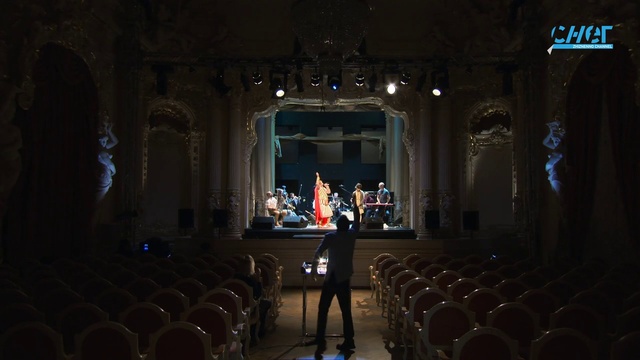 Video Reference: Chair, Hall, Entertainment, Event, Darkness, Building, Performing arts center, Musical instrument accessory, Suit, Theatre