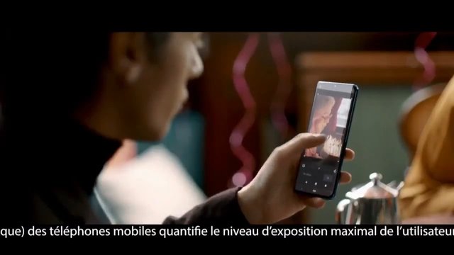 Video Reference: smartphone, mobile phone, person, screen, indoor, close up, handheld, subtitle, French text, technology, video frame, blurred background