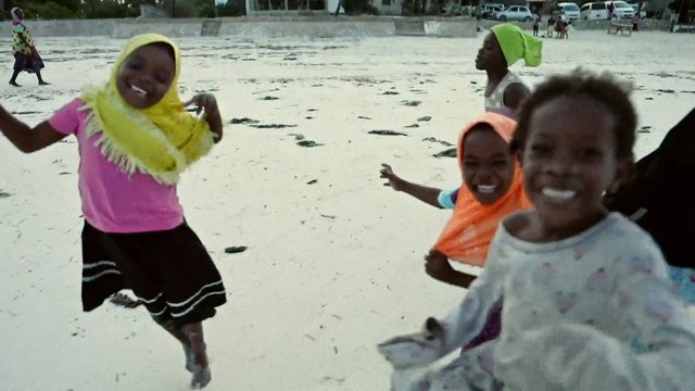 Video Reference: children, beach, running, playing, smiling, sand, outdoors, group, hijab, shoreline, daytime, motion, vacation, recreation, people, coastal