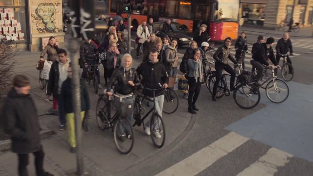 Video Reference: urban, street, crosswalk, pedestrians, cyclists, bicycles, commute, traffic, city, crowd, intersection, public transport, daytime, outdoor
