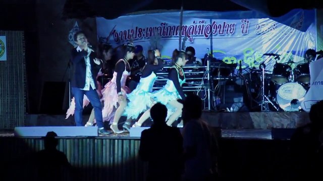 Video Reference: stage performance, live concert, singer, dancers, music event, audience, night scene, indoor stage, costumes, drums, entertainment, performance lighting, banner, crowd silhouettes