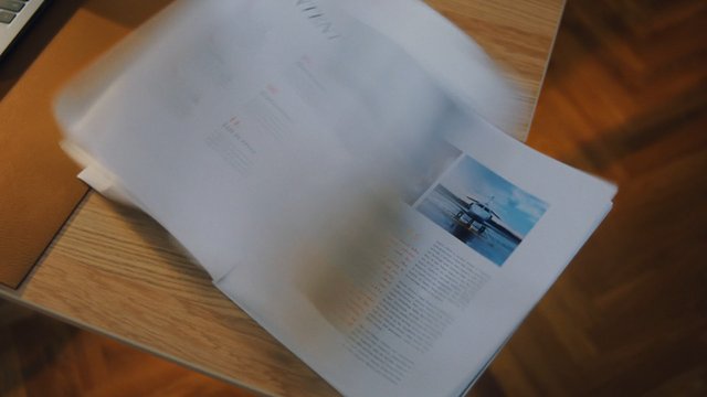 Video Reference: document, paper, pages, book, flip, blurred, desk, wooden table, printed text, airplane photo, close-up, motion blur, office, reading