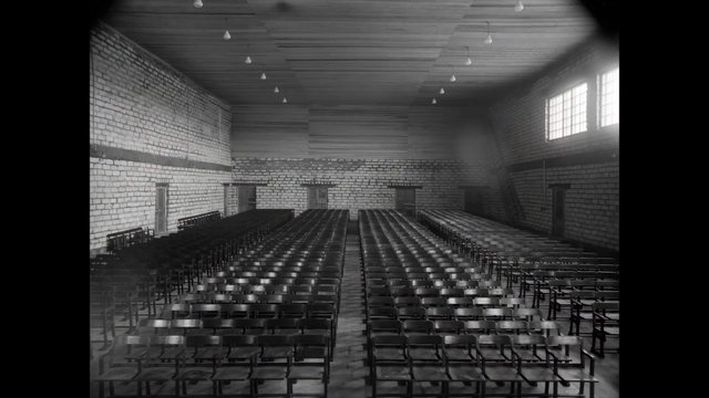 Video Reference: empty hall, chairs, indoor, black and white, brick walls, auditorium, rows, industrial interior, windows, ceiling lights, symmetry, wide angle