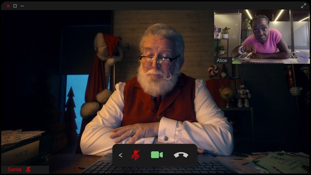 Video Reference: video call, Santa, older man, desk, office, inset window, woman, computer screen, mute, camera, call controls, holiday, indoor, dim lighting, desktop, remote meeting