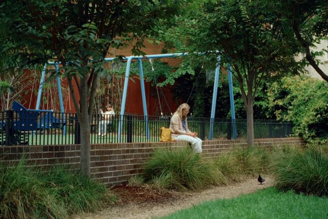 Video Reference: park, playground, woman, sitting, trees, outdoors, greenery, bench, child, suburban, garden, daylight, leisure, play area