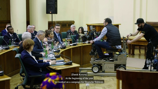 Video Reference: Furniture, Table, Chair, Engineering, Event, Suit, Microphone, Government, Job, Conversation