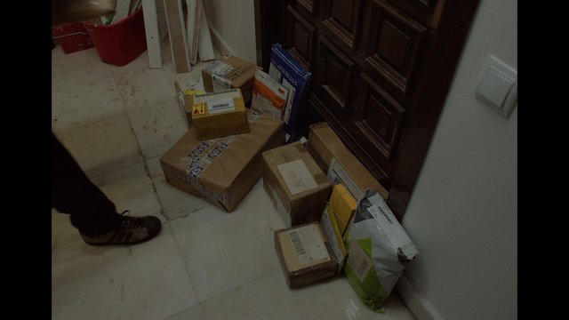 Video Reference: packages, parcels, shipping boxes, delivery, doorway, indoor, floor, cardboard, mail, entryway, home interior, stacked boxes