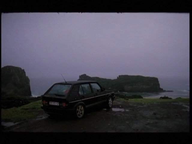 Video Reference: car, hatchback, coast, cliff, ocean, overcast, wet, landscape, road, parked, outdoors, travel, scenic, foggy, dusk, shoreline