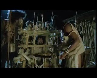 Video Reference: dimly lit, people, wooden cage, spears, indoor, crowd, dark room, historical, primitive structure, standing figures, rural, suspense, group scene, wooden bars, low light