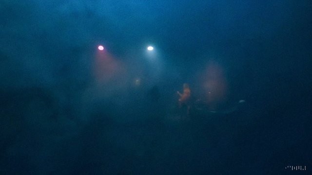 Video Reference: dark, stage, concert, spotlights, haze, smoke, performance, live music, indistinct figures, low light, blue lighting, indoor, night, atmospheric