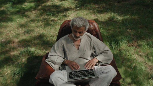 Video Reference: older man, laptop, outdoor, grass, chair, sitting, working, technology, casual clothing, nature, top view, alone, daylight