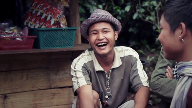 Video Reference: outdoors, people, laughing, conversation, man, hat, wooden stall, casual clothing, smiling, group, village, market, seated, daytime