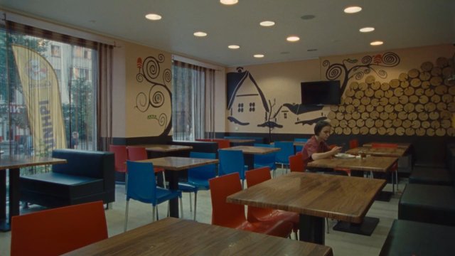 Video Reference: cafe, restaurant, interior, empty tables, chairs, wooden tables, indoor, dining area, person, modern decor, windows, wall mural, seating, casual
