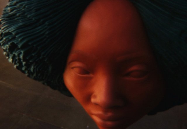 Video Reference: sculpture, face, close-up, abstract, stylized, portrait, red light, dark background, art, texture, human face, headdress, moody, macro, decorative, figurine