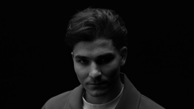 Video Reference: portrait, black and white, close-up, young man, studio, dark background, face, fashion, moody, minimal, headshot