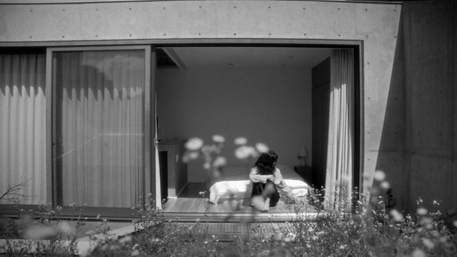 Video Reference: black and white, modern house, bedroom, sliding door, interior, person sitting, bed, architecture, foreground flowers, minimalist, window, curtains, contemporary, home