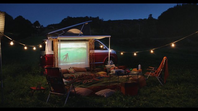 Video Reference: camping, van, vanlife, outdoor, night, string lights, projection screen, surfer, grassy field, recreation, travel, relaxation, camping chairs, portable projector, off-grid, evening