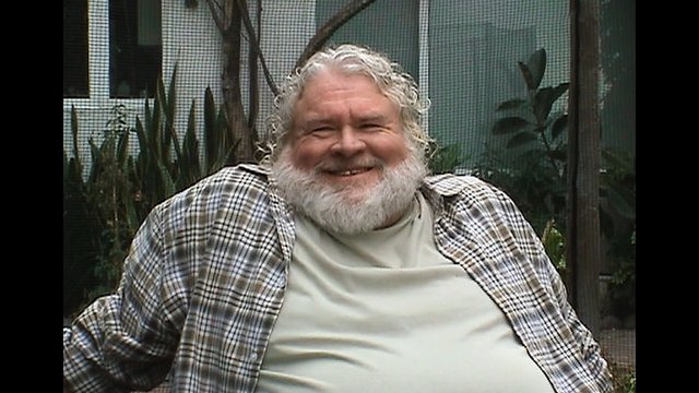 Video Reference: older man, smiling, beard, plaid shirt, outdoors, portrait, seated, garden, interview, casual, middle close-up