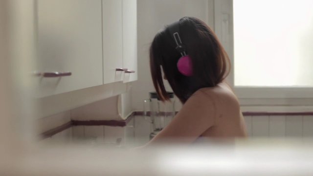 Video Reference: person, headphones, indoors, kitchen, window, back view, short hair, seated, home interior, soft light, casual, audio, listening, daily life