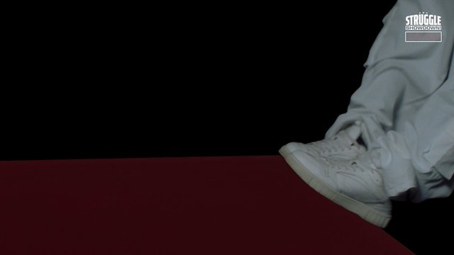 Video Reference: sneaker, shoe, footwear, leg, pants, close-up, dark background, red floor, studio shot, partial person, motion, fashion, casual