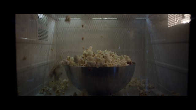 Video Reference: popcorn, microwave, bowl, snack, cooking, kitchen, food, appliance, indoor, close-up, through screen, metal bowl