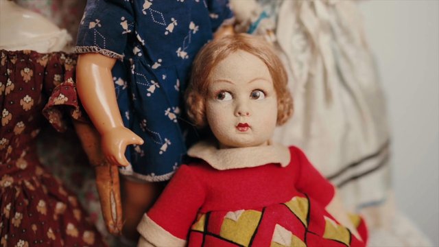 Video Reference: vintage doll, antique toy, porcelain doll, close-up, indoor, still life, collectible, old toy, red dress, blue dress, handmade, playroom, nostalgia