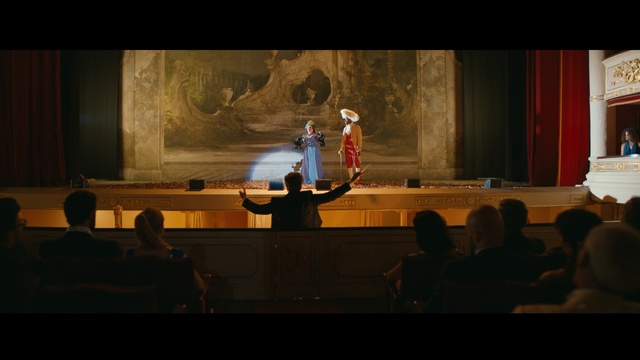 Video Reference: Entertainment, Curtain, Performing arts, Chair, Event, Projection screen, Stage, Performance art, Suit, Theatre