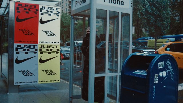 Video Reference: street, phone booth, person, mailbox, graffiti, urban, advertising, posters, cars, bus, sidewalk, city, glass, Nike, outdoor