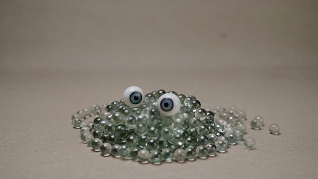 Video Reference: glass beads, toy eyes, frog face, craft, abstract, close-up, still life, beads, green, beige background, playful, handmade, minimal, odd object