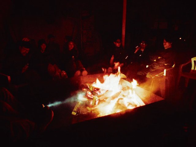 Video Reference: fire, people, night, group, campfire, gathering, dark, indoor, warm light, social, smoke, flames, sitting, conversation