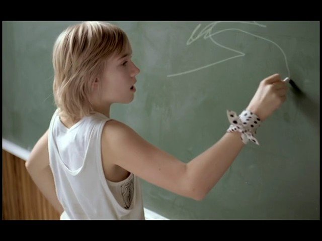 Video Reference: classroom, chalkboard, chalk, student, writing, school, education, green board, side view, young person, white shirt, indoor, learning, lesson