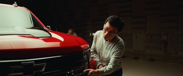 Video Reference: man, car repair, truck, pickup truck, garage, workshop, mechanic, vehicle, front grille, red car, maintenance, indoor, glasses, hands-on, automotive, close-up