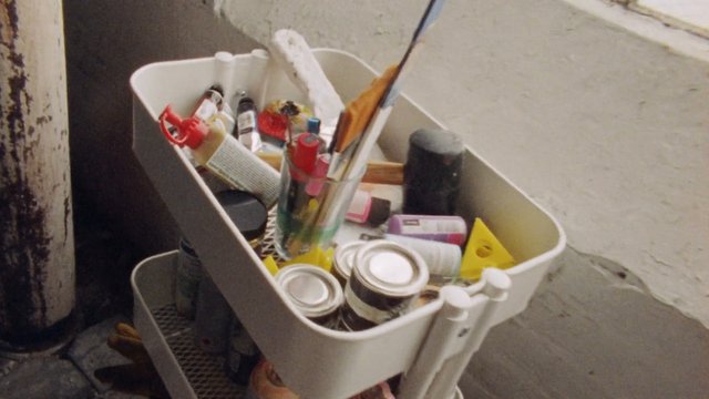 Video Reference: storage cart, household items, bottles, jars, brushes, organizer, clutter, interior, wall, doorway, supplies, plastic container, metal cup, home storage