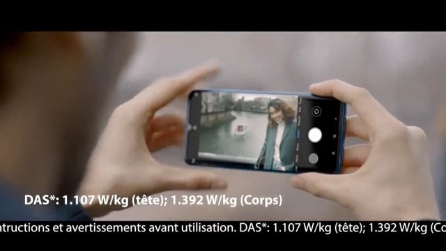 Video Reference: smartphone, phone camera, hands, outdoor, woman, selfie, video recording, mobile device, close-up, screen, advertisement, French text, disclaimer, technology