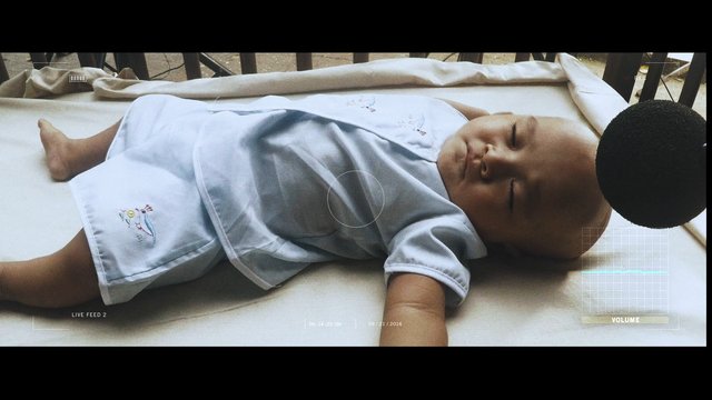 Video Reference: baby, infant, sleeping, lying down, padded surface, light blue clothing, indoor, close-up, camera overlay, recording, resting, portrait