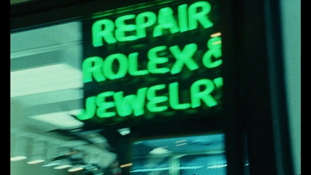 Video Reference: repair, storefront, neon sign, green, signage, shop, window, indoor, blur, close-up, text, commercial, retail