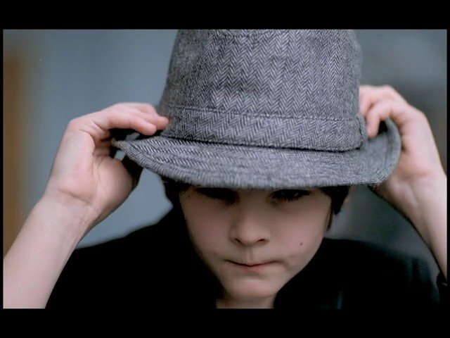 Video Reference: child, hat, fedora, gray, hands, portrait, close-up, adjusting, brim, plain background, indoor, face, clothing, youth
