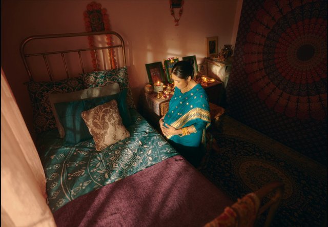 Video Reference: pregnant, woman, sari, bedroom, candles, home interior, portrait, expecting mother, traditional clothing, religious decor, warm lighting, domestic scene, bed, indian decor, interior design