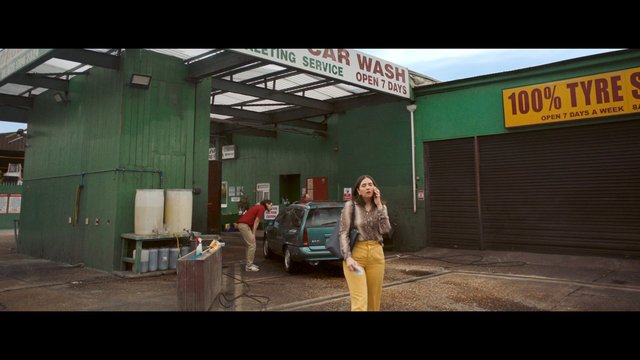 Video Reference: car wash, tire service, outdoor, garage, parked car, hatchback, phone call, woman, man, service bay, signage, wet ground, commercial building, street scene