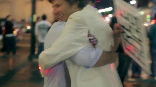 Video Reference: hug, embrace, night, street, city, people, outdoors, blurry, motion, lights, pedestrians, urban, social, celebration